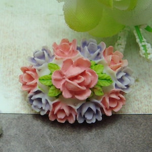 Op de afbeelding: Een cluster van roze en paarse bloemen van stof met groene bladeren. De bloemen zijn in een cirkelvormige vorm gerangschikt en hebben een wit midden.