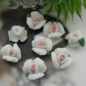 May include: Ten white ceramic roses with pink centres. The roses have green leaves.