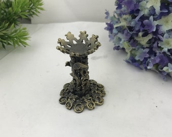 May include: A decorative metal stand with an ornate design featuring a bird and floral motifs. The stand has a round top and a base with intricate details.