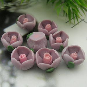 Könnte beinhalten: Eine Sammlung von acht kleinen, lila, blumenförmigen Dekorationen mit rosafarbenen Zentren. Die Dekorationen bestehen aus einem weichen, formbaren Material und eignen sich perfekt, um jedem Bastelprojekt einen Hauch von Verspieltheit zu verleihen.