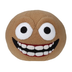 May include: A soft, plush toy in the shape of a smiling face. The toy is tan with large white eyes and black pupils. It features a wide grin with red gums and white teeth. The toy has a round shape and is made of a soft material.