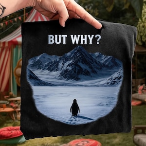 Könnte beinhalten: Schwarzes T-Shirt mit einem Pinguin, der auf Schnee auf eine Bergkette zugeht. Der Text "BUT WHY?" steht in Silber über dem Bild. Das Design ist von einem dunklen Rand umgeben.