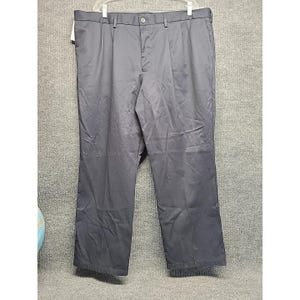 May include: Dark grey pleated trousers hanging on a hanger. The trousers have a button closure, belt loops, and pockets. The fabric appears to be wrinkle-resistant. The trousers are a size 48.