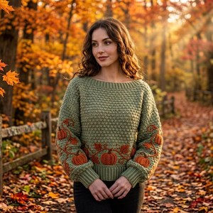 Puede incluir: Un su&eacute;ter de punto de color verde salvia con mangas largas, que presenta un patr&oacute;n de textura de panal en el cuerpo y las mangas, decorado con calabazas naranjas y enredaderas marrones bordadas a lo largo del dobladillo y los pu&ntilde;os.