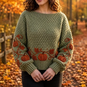 May include: A sage green long-sleeve sweater featuring a textured crochet knit pattern. The garment is decorated with embroidered orange pumpkins and brown vines that wrap around the sleeves and across the lower front section of the sweater.