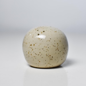 Puede incluir: Un salero esférico de cerámica moteada. El salero blanquecino tiene pequeñas manchas marrones y un acabado brillante. La forma redonda y la paleta de colores neutros lo convierten en un complemento versátil para cualquier cocina o mesa de comedor.