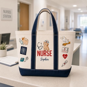 May include: Cream-colored tote bag with navy blue accents and handles. The bag features a design with a cartoon kitten wearing a nurse's cap, a stethoscope, and the word "NURSE" in red. Additional medical-themed graphics are included.