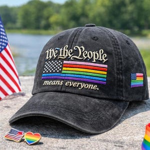 May include: A black baseball cap with the embroidered phrase "We the People means everyone." The cap features a rainbow flag design and a small American flag patch. The cap is made of a worn, faded material.