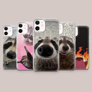 May include: Five phone cases with raccoon-themed designs. The cases showcase close-up images of raccoons with different expressions, including one wearing sunglasses and another with a fiery background. The cases are clear with a glossy finish.