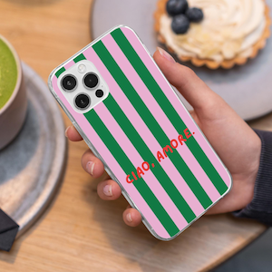 May include: Clear phone case with a pink and green striped pattern. The case has the words "CIAO, AMORE." in red. The phone case is held in a hand.