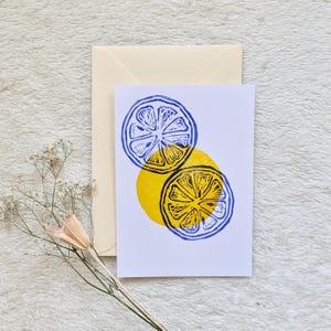 Könnte beinhalten: Eine Grußkarte mit einem Zitronenscheiben-Design. Die Karte zeigt zwei Zitronenscheiben-Illustrationen in Blau und Gelb, mit einem gelben Kreis darunter. Ein Umschlag befindet sich hinter der Karte.