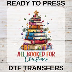 May include: A DTF transfer design showing a Christmas tree constructed from stacked books, adorned with baubles and a gold star. The text "ALL BOOKED FOR Christmas" is below the tree, with "READY TO PRESS" and "DTF TRANSFERS" above and below the image.