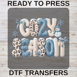 May include: A graphic design featuring the words "COZY SEASON" in a knitted font, with a snowman and snowflakes. The word "COZY" has a leopard print pattern. The text "READY TO PRESS" and "DTF TRANSFERS" are at the top and bottom.