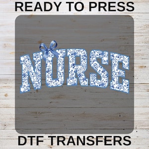 May include: A DTF transfer ready to press, displaying the word "NURSE" in large, stylized letters. The letters are filled with a blue and white floral pattern and topped with a blue bow. The text "READY TO PRESS" and "DTF TRANSFERS" are above and below the main text.
