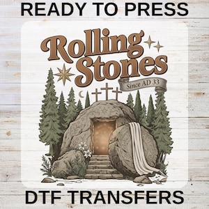 May include: A DTF transfer design with the text "READY TO PRESS" at the top and "DTF TRANSFERS" at the bottom. The design features the words "Rolling Stones" in a brown, vintage font, with an illustration of a tomb and crosses.