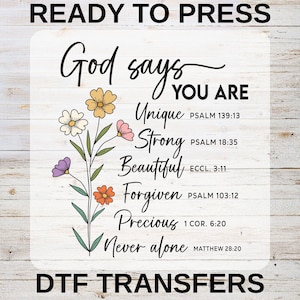 Peut inclure: Un motif de transfert DTF avec le texte "Dieu dit QUE VOUS ÊTES Unique, Fort, Beau, Pardonné, Précieux, Jamais seul." Accents floraux en jaune, blanc, rose, orange et violet. Les mots "READY TO PRESS" et "DTF TRANSFERS" sont également inclus.