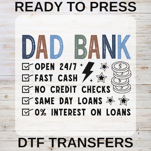 May include: A DTF transfer design with the words "DAD BANK" in blue, brown, and green. The design includes icons and text such as "OPEN 24/7", "FAST CASH", and "0% INTEREST ON LOANS". The words "READY TO PRESS" and "DTF TRANSFERS" are also included.