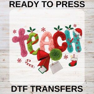 May include: A colorful DTF transfer design with the word "TEACH" in a festive, textured style. The design includes a pink cross, green and red letters, snowflakes, a bow, and a Santa hat. The text "READY TO PRESS" and "DTF TRANSFERS" are also included.