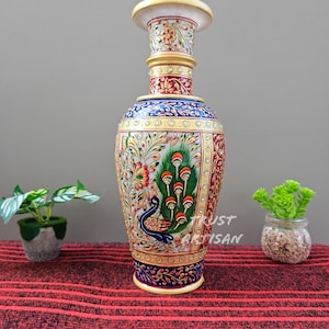 May include: A tall, ornate marble vase with a peacock design. The vase features a cream-colored top and base, with intricate floral and peacock feather patterns in red, blue, and gold. The vase is a decorative item.