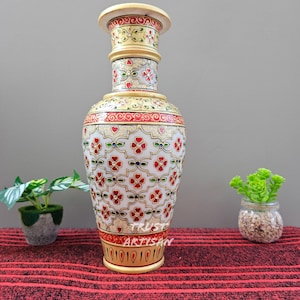 Puede incluir: Un jarrón decorativo con base crema y detallados diseños florales en rojo, verde y dorado. El jarrón tiene una base ancha y una parte superior acampanada, y mide aproximadamente 30 cm de altura.