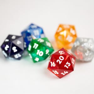 May include: A collection of colorful polyhedral dice, including red, green, blue, orange, gray, and purple. Each die features white numbering. The dice are arranged on a white surface, ideal for tabletop gaming.