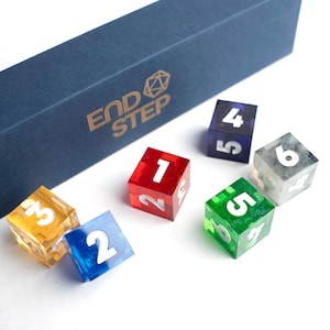 May include: A set of colorful, translucent dice with white numbering, including red, green, blue, purple, yellow, and clear. The dice are scattered near a navy blue box with the gold text "END STEP".