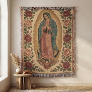 May include: A rectangular woven tapestry featuring a central image of the Virgin of Guadalupe in a blue mantle and pink robe, surrounded by a golden sunburst. The border is decorated with red and pink roses, finished with a fringed edge.