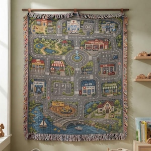 May include: A woven tapestry blanket featuring a colorful city map design with roads, a hospital, a fire station, a gas station, a car wash, a post office, a pet shop, a construction zone, a bridge, a pond, and a fountain with fringed edges.