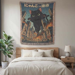 May include: Woven tapestry featuring a giant black cat destroying a city. The cat has green eyes and pink ears. The tapestry has a blue and beige color scheme with Japanese text at the top. The buildings are on fire.