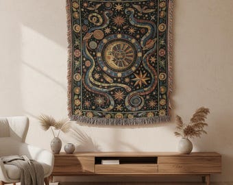 May include: A black tapestry with a celestial design featuring a crescent moon, sun, stars, and swirling patterns in shades of blue, yellow, and orange. The tapestry has a fringed edge and is hanging on a beige wall. The tapestry is a decorative home decor item.