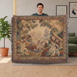 May include: A tapestry throw blanket featuring a detailed landscape scene with a heron near a body of water. The blanket has a fringed edge and a color palette of greens, browns, and beige.