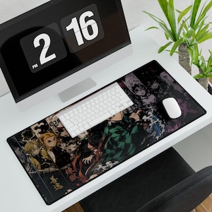 Può includere: Un tappetino da scrivania rettangolare nero con un design colorato di personaggi anime. Una tastiera e un mouse bianchi sono sul tappetino, con un monitor di computer che mostra l'ora sullo sfondo. Una pianta verde è a destra.