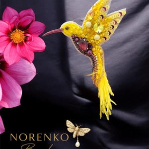 Puede incluir: Un broche de colibrí amarillo hecho a mano con intrincados abalorios y detalles de joyas. El broche presenta un pico largo y delgado y una cola de plumas amarillas. También es visible un broche de polilla dorado más pequeño con una perla colgante. Se muestra el texto "NORENKO Brooches".