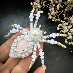Puede incluir: Broche de araña con cuentas hecho a mano, blanco, rosa y amarillo. El cuerpo de la araña presenta una gran piedra rosa y una perla central. Las patas están hechas de cuentas de varios colores. Accesorio único.
