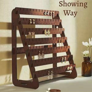 May include: A dark brown wooden earring display stand with multiple horizontal rows of slots for hanging earrings. The stand is angled and holds various styles of earrings, including studs and dangling designs. The text "Showing Way" is visible.