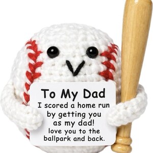 May include: A white crocheted baseball with red stitching, black bead eyes, and a black yarn mouth. It holds a small wooden baseball bat and a white sign that reads: To My Dad, I scored a home run by getting you as my dad! love you to the ballpark and back.