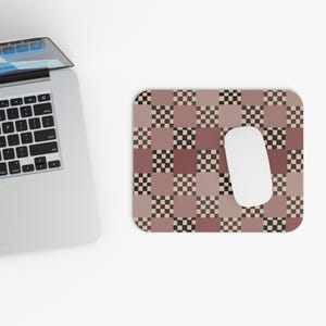 Può includere: Un mouse per computer e un tappetino per mouse a fantasia. Il tappetino per mouse presenta un motivo a scacchiera nei toni del marrone, beige e nero. Un mouse per computer bianco è posizionato sul lato destro del tappetino per mouse. Un laptop è visibile nell'angolo in alto a sinistra.