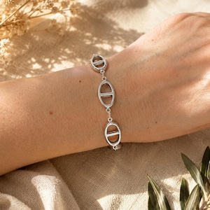 Peut inclure: Un bracelet à chaîne de couleur argentée composé d'une série de maillons ovales répétitifs, chacun doté d'une barre horizontale au centre. Le bracelet est constitué de composants en métal poli reliés par de petits anneaux circulaires.