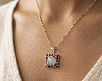 May include: A gold chain necklace featuring a square pendant with a central faceted light blue stone surrounded by a border of small, round, deep purple stones. The pendant is suspended from a delicate gold link chain that rests against the neck.