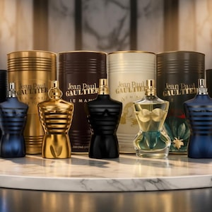 May include: A collection of Jean Paul Gaultier fragrances, featuring bottles in various colors including gold, black, and blue. The bottles are in the shape of a torso, with matching cylindrical containers behind them. The text "Jean Paul Gaultier" is visible.