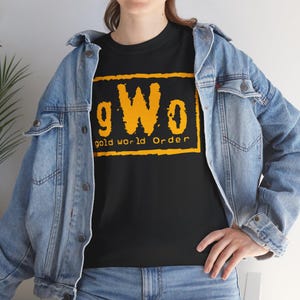 May include: Black t-shirt with the text "gWo gold world Order" in a yellow, rectangular design. The shirt is worn with a blue denim jacket and jeans.
