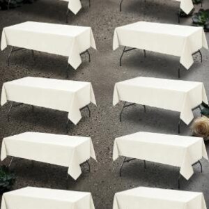 May include: A set of ten rectangular folding tables, each covered with a solid off-white tablecloth. The tables feature black metal legs and are arranged in two vertical columns of five, providing a uniform display of event furniture.