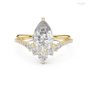 May include: A gold engagement ring with a pear-shaped diamond center stone. The ring features a delicate band and a curved row of smaller diamonds. The ring is set against a white background.