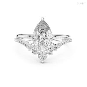May include: A sparkling engagement ring with a pear-shaped diamond as the centerpiece. The ring features a delicate band and a halo of smaller diamonds, creating a glamorous and elegant design. The ring is set in a silver metal.