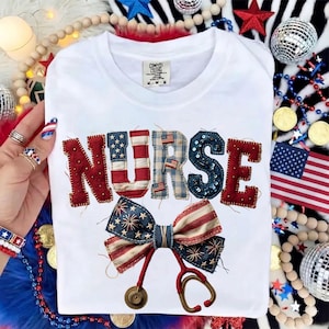 May include: White t-shirt with the word "NURSE" in red, blue, and sequined letters. A bow tie and stethoscope design are below the word. The bow tie has a patriotic design. The shirt has a Comfort Colors tag.