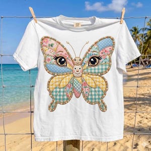 Peut inclure: T-shirt blanc avec un motif de papillon coloré. Les ailes du papillon sont un patchwork de motifs floraux, à pois et vichy en rose, bleu, jaune et vert. Le t-shirt est suspendu à une corde à linge.