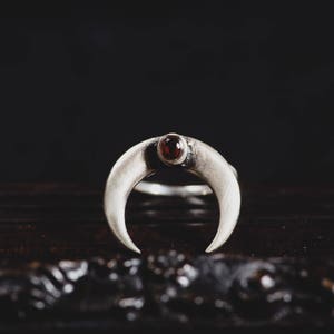 Può includere: Un anello d'argento a forma di mezzaluna con una pietra rossa al centro.