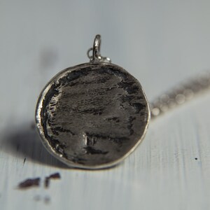 May include: A silver pendant with a round, textured surface. The pendant is attached to a silver chain.