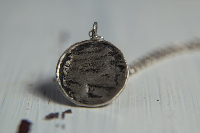 May include: A silver pendant with a round, textured surface. The pendant is attached to a silver chain.