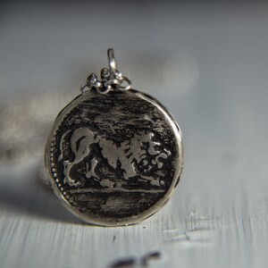 May include: A silver pendant with a detailed lion design. The pendant is round and has a textured surface.
